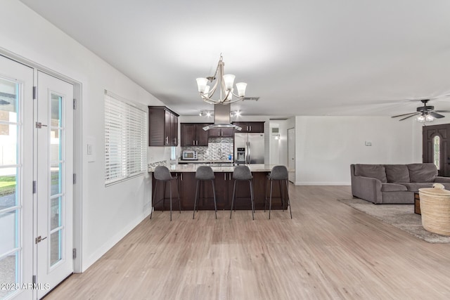 kitchen with decorative backsplash, kitchen peninsula, stainless steel fridge, island range hood, and dark brown cabinets