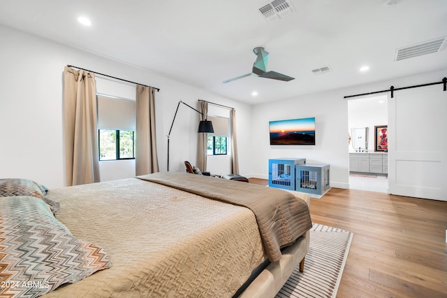 bedroom with light wood-type flooring, a barn door, and ceiling fan