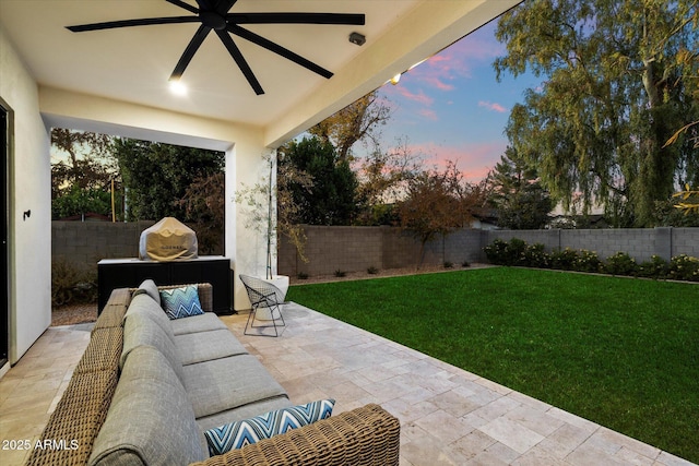 patio terrace at dusk with outdoor lounge area, ceiling fan, and a yard