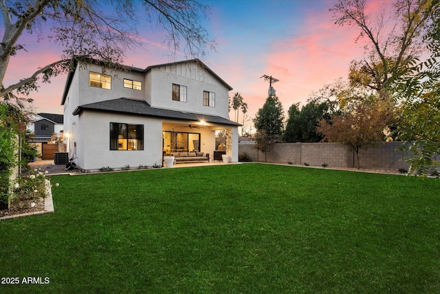 back house at dusk with a lawn, central air condition unit, ceiling fan, and an outdoor hangout area