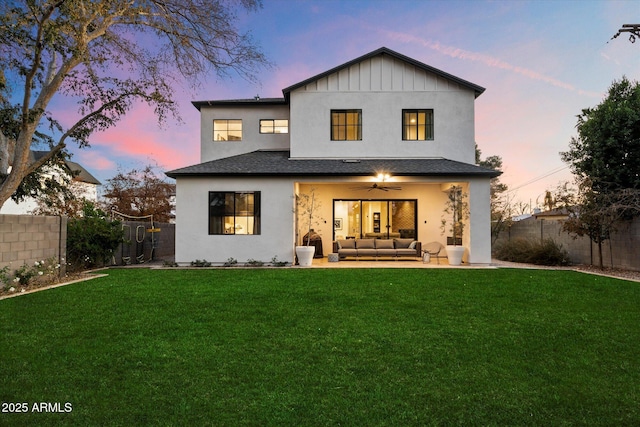 back house at dusk with an outdoor hangout area, a patio, ceiling fan, and a lawn