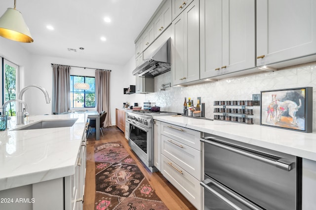 kitchen with light stone countertops, appliances with stainless steel finishes, sink, wood-type flooring, and hanging light fixtures