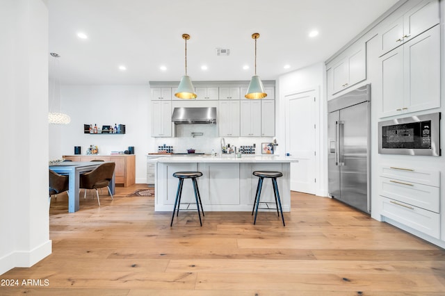 kitchen with extractor fan, pendant lighting, built in appliances, light hardwood / wood-style flooring, and a breakfast bar area