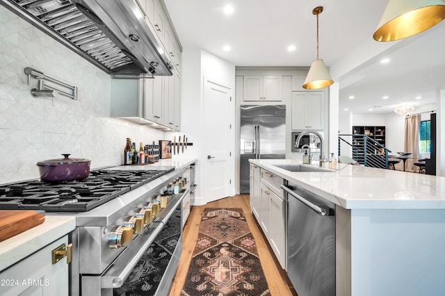 kitchen with sink, wall chimney range hood, tasteful backsplash, light hardwood / wood-style floors, and high end appliances