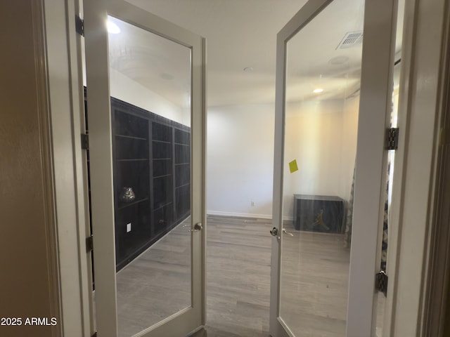 hall featuring visible vents, baseboards, and wood finished floors
