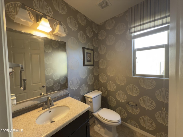 half bathroom featuring vanity, visible vents, toilet, tile patterned floors, and wallpapered walls