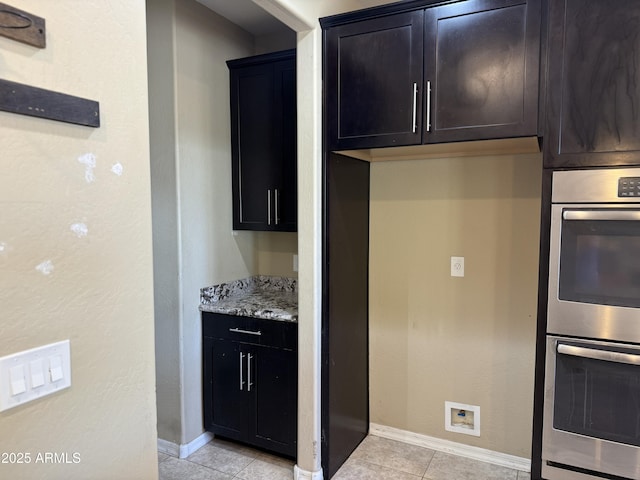 kitchen with light tile patterned floors, baseboards, double oven, and light stone countertops