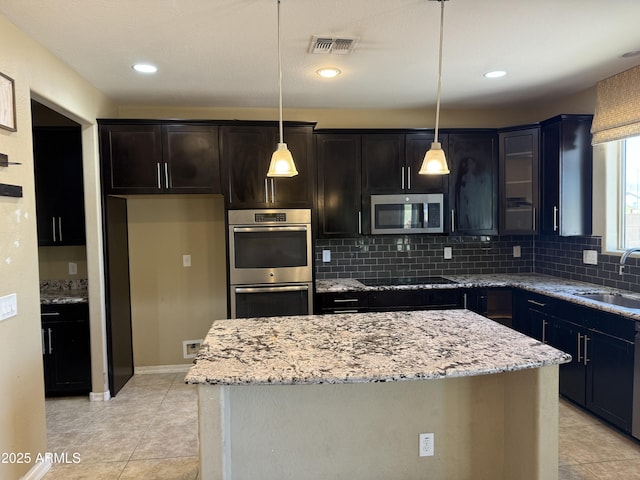 kitchen with tasteful backsplash, a center island, light stone countertops, visible vents, and stainless steel appliances
