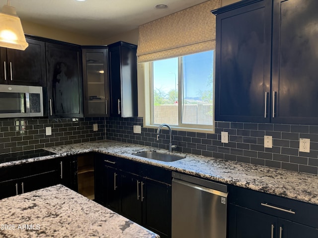 kitchen with appliances with stainless steel finishes, a sink, backsplash, and light stone counters