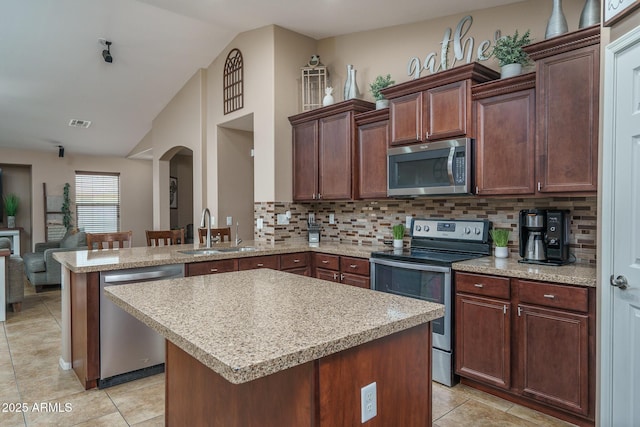 kitchen with sink, appliances with stainless steel finishes, a center island, vaulted ceiling, and kitchen peninsula