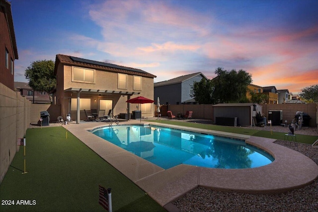 pool at dusk featuring a shed, a pergola, a patio, and grilling area