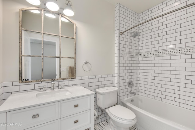 full bathroom with tiled shower / bath, vanity, toilet, and tile walls