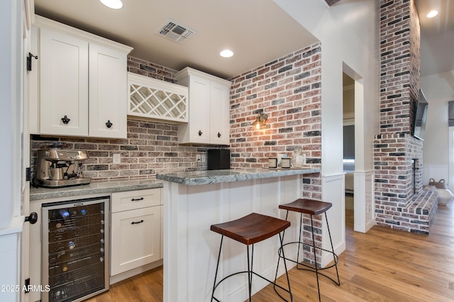 kitchen with white cabinetry, light stone countertops, beverage cooler, and a kitchen bar