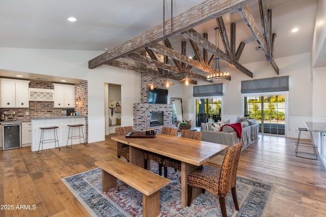 dining area featuring a brick fireplace, light wood-type flooring, beamed ceiling, a towering ceiling, and beverage cooler