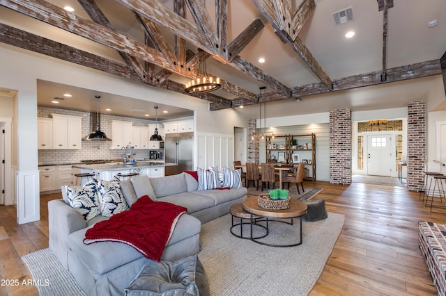 living room with beam ceiling, a towering ceiling, an inviting chandelier, and light wood-type flooring