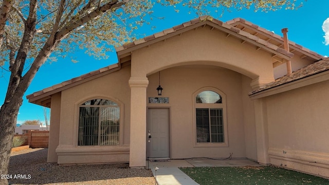 entrance to property featuring a tile roof, fence, and stucco siding