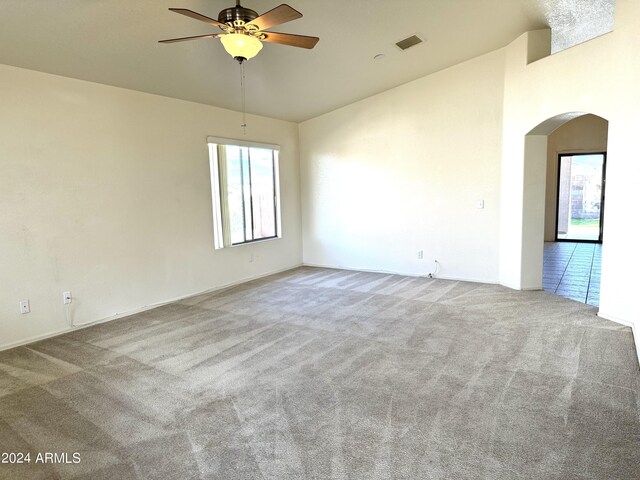 carpeted empty room with arched walkways, ceiling fan, high vaulted ceiling, and visible vents