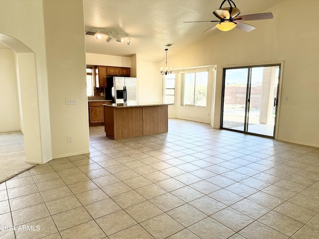 kitchen featuring arched walkways, light tile patterned floors, open floor plan, stainless steel fridge, and ceiling fan with notable chandelier