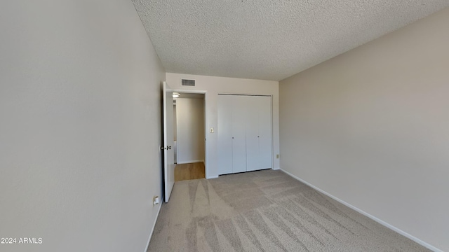 unfurnished bedroom with a textured ceiling, light carpet, visible vents, baseboards, and a closet