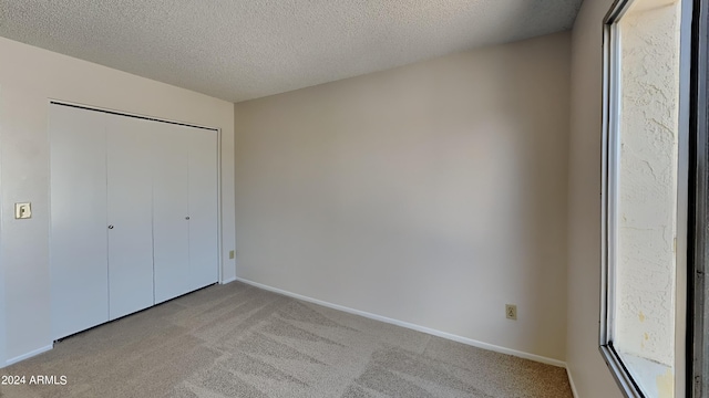 unfurnished bedroom featuring a closet, light carpet, a textured ceiling, and baseboards