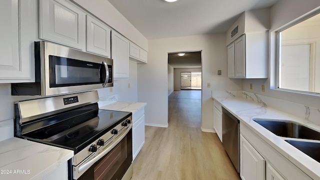 kitchen with appliances with stainless steel finishes, white cabinetry, light wood-type flooring, and a healthy amount of sunlight