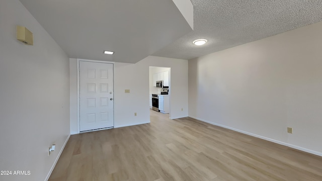 empty room with light wood-type flooring, baseboards, and a textured ceiling