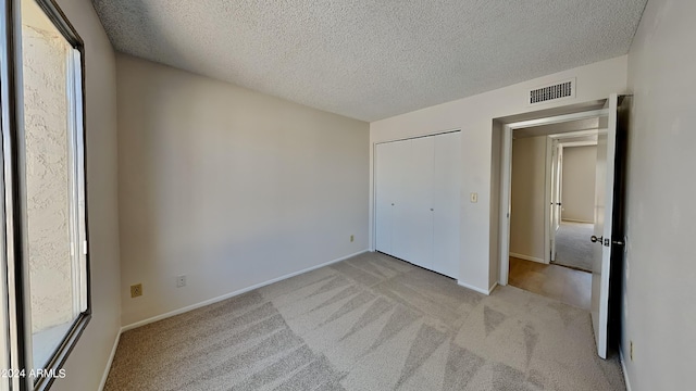 unfurnished bedroom featuring light carpet, baseboards, visible vents, and a textured ceiling