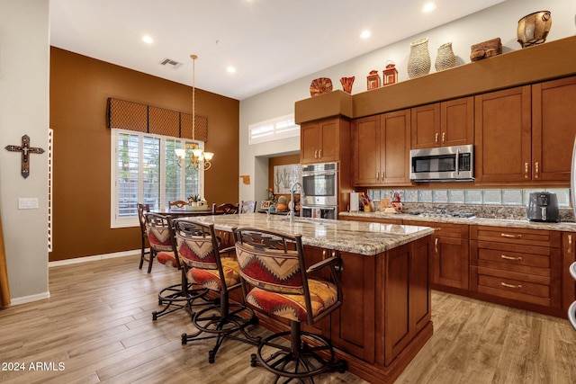 kitchen featuring hanging light fixtures, a kitchen breakfast bar, a kitchen island with sink, light hardwood / wood-style flooring, and stainless steel appliances