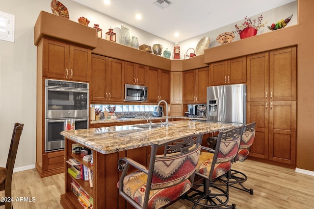 kitchen featuring a kitchen island with sink, sink, light stone countertops, appliances with stainless steel finishes, and light hardwood / wood-style floors