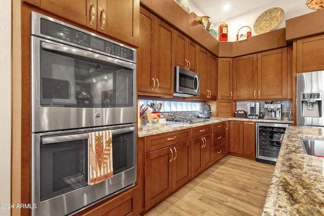 kitchen featuring appliances with stainless steel finishes, wine cooler, light stone countertops, and light wood-type flooring