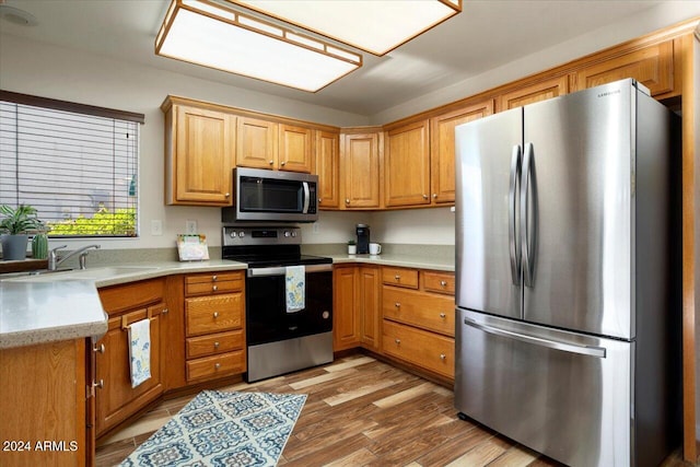 kitchen with stainless steel appliances, sink, and light hardwood / wood-style flooring