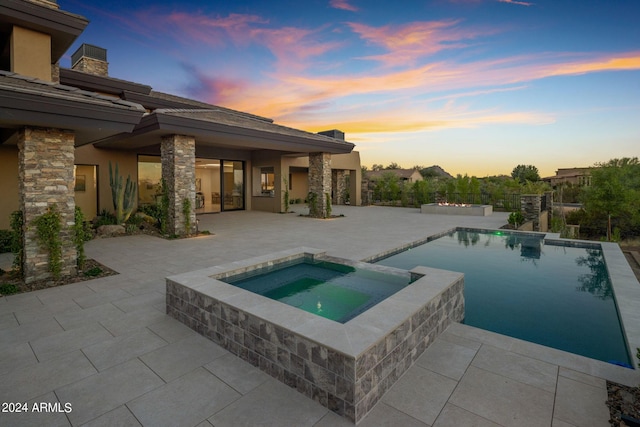 pool at dusk featuring an in ground hot tub and a patio