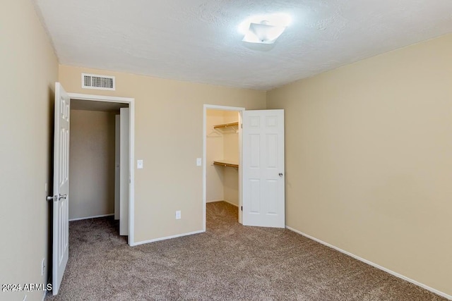 unfurnished bedroom featuring a walk in closet, a closet, light colored carpet, and a textured ceiling