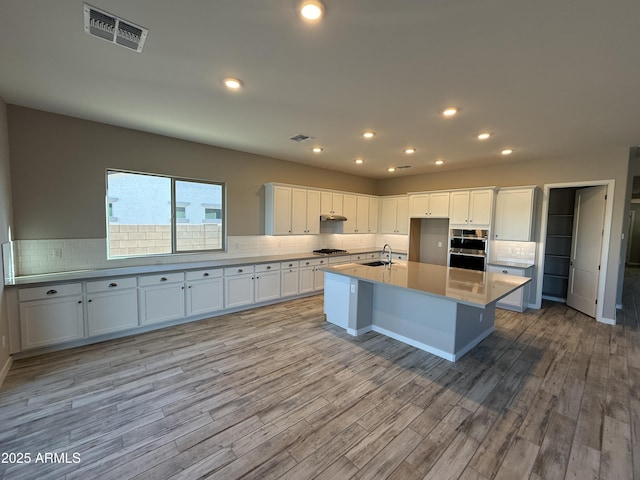 kitchen featuring sink, a kitchen island with sink, light hardwood / wood-style floors, and white cabinetry