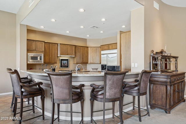 kitchen featuring a kitchen bar, built in appliances, kitchen peninsula, and light stone countertops