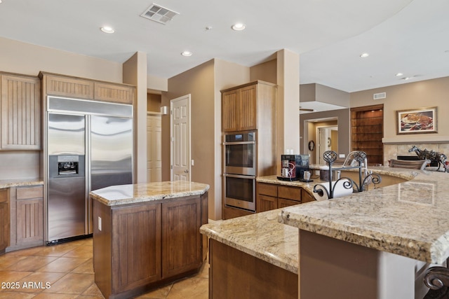 kitchen featuring light tile patterned floors, stainless steel appliances, a center island, light stone counters, and kitchen peninsula