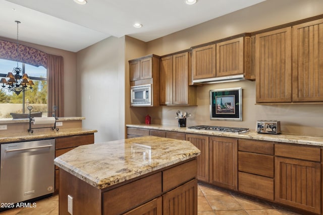 kitchen featuring an inviting chandelier, hanging light fixtures, appliances with stainless steel finishes, a kitchen island, and light stone countertops