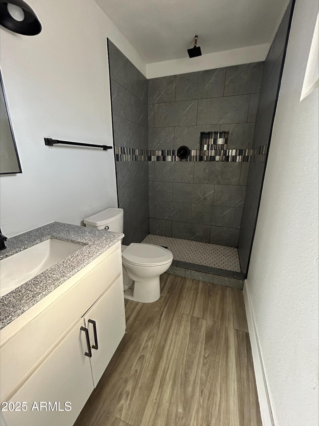 full bath featuring vanity, a tile shower, toilet, and wood finished floors