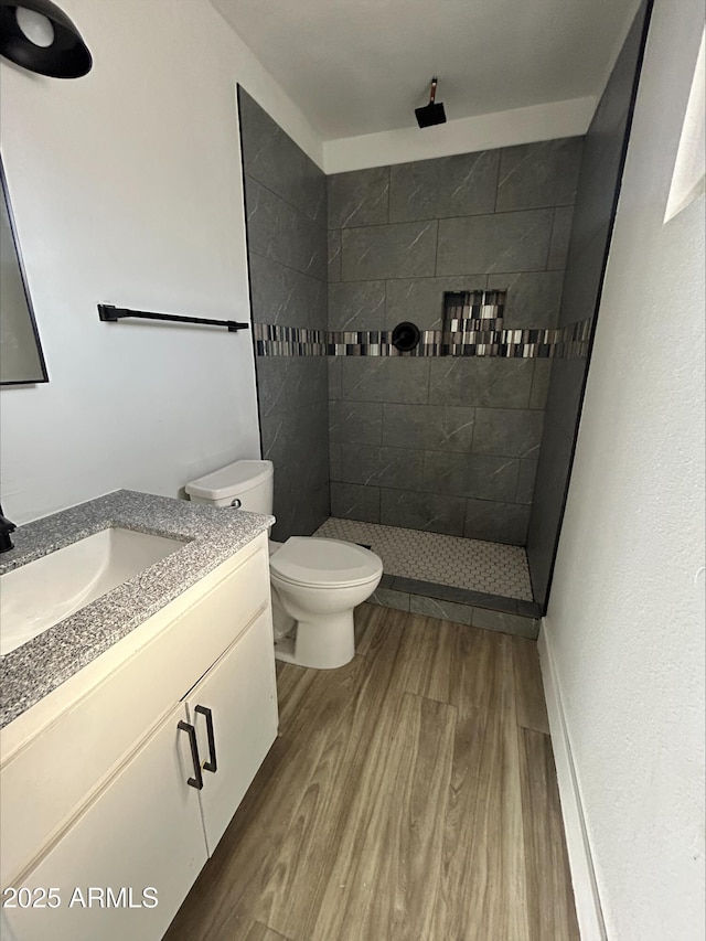 full bath featuring vanity, a tile shower, toilet, and wood finished floors