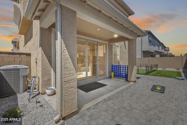 property entrance featuring a patio area, fence, stucco siding, and central air condition unit