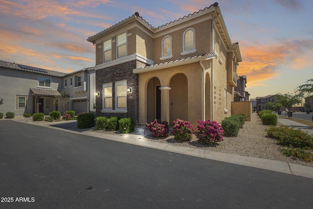 mediterranean / spanish home featuring stucco siding, stone siding, an attached garage, and a tile roof