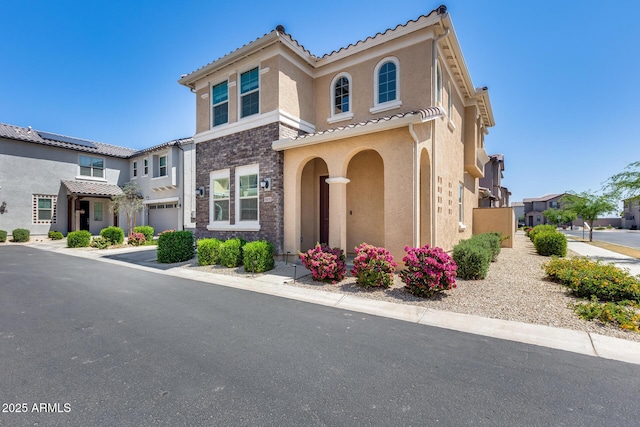 mediterranean / spanish home featuring a tiled roof, stone siding, a garage, and stucco siding