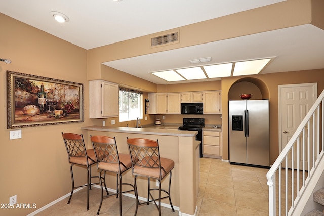 kitchen with a peninsula, a breakfast bar, visible vents, light countertops, and black appliances