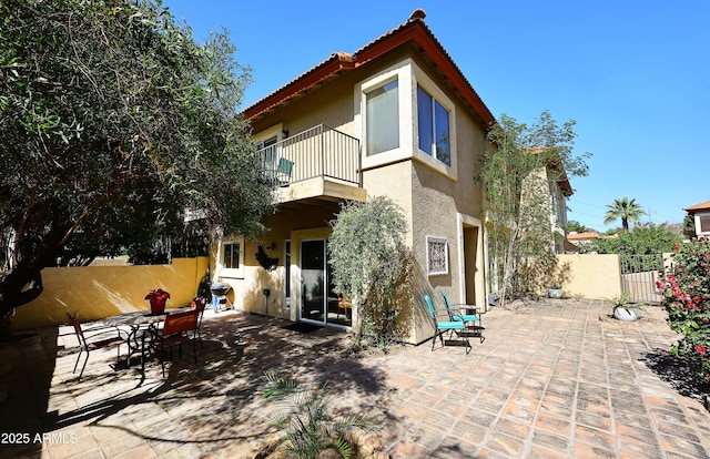 rear view of property featuring a balcony, a tiled roof, fence, a patio area, and stucco siding