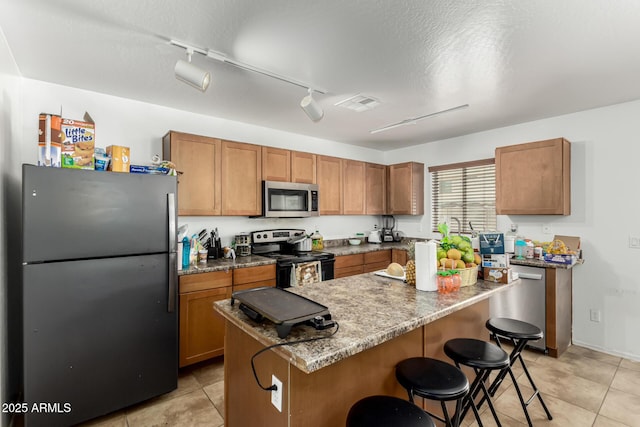 9236 N 184th Ln, Waddell, AZ 85355 - kitchen featuring stainless steel appliances, a kitchen bar, light tile patterned flooring, and brown cabinetry