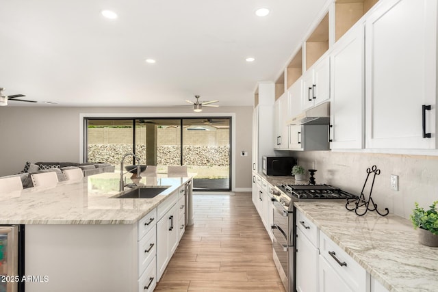 kitchen with under cabinet range hood, double oven range, ceiling fan, a sink, and a kitchen island with sink