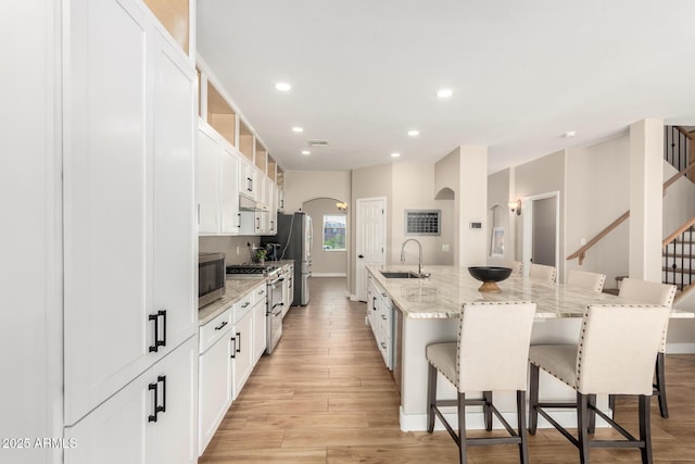 kitchen featuring a breakfast bar, a sink, arched walkways, stainless steel appliances, and a large island with sink