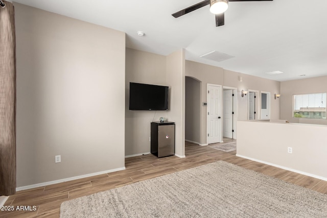 unfurnished living room with arched walkways, baseboards, ceiling fan, and wood finished floors