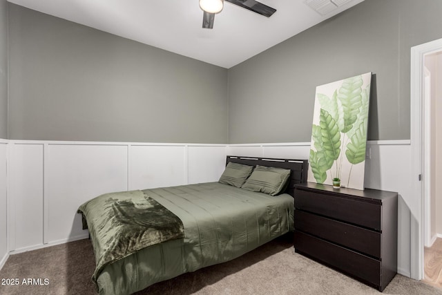 carpeted bedroom with wainscoting, a decorative wall, a ceiling fan, and visible vents