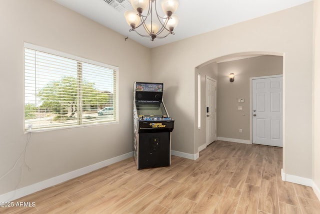 interior space with light wood-style flooring, visible vents, baseboards, arched walkways, and a chandelier